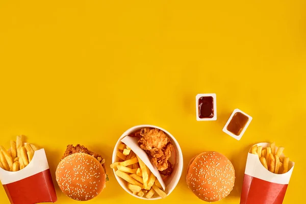 Fast food dish top view. Meat burger, potato chips and wedges. Take away composition. French fries, hamburger, mayonnaise and ketchup sauces on yellow background.