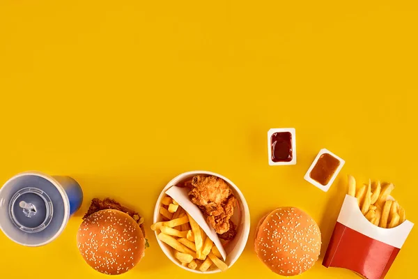 Fast food tepesi manzarası. Et burger, patates cipsi ve kama. Kompozisyonu kaldır. Patates kızartması, hamburger, mayonez ve sarı arka planda ketçap sosu.. — Stok fotoğraf