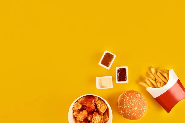 Plat de restauration rapide vue du dessus. Burger de viande, croustilles et quartiers. Retirer la composition. Frites, hamburger, mayonnaise et sauces ketchup sur fond jaune. — Photo