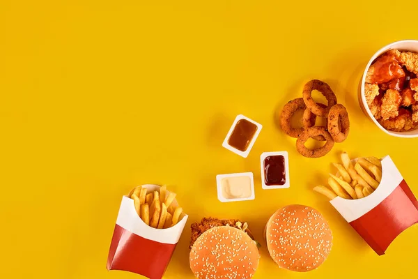 Fast food tepesi manzarası. Et burger, patates cipsi ve kama. Kompozisyonu kaldır. Patates kızartması, hamburger, mayonez ve sarı arka planda ketçap sosu.. — Stok fotoğraf
