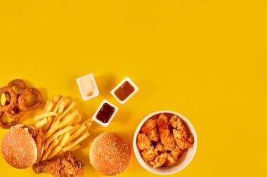 Fast food tepesi manzarası. Et burger, patates cipsi ve kama. Kompozisyonu kaldır. Patates kızartması, hamburger, mayonez ve sarı arka planda ketçap sosu..