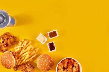 Fast food tepesi manzarası. Et burger, patates cipsi ve kama. Kompozisyonu kaldır. Patates kızartması, hamburger, mayonez ve sarı arka planda ketçap sosu..