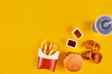 Fast food tepesi manzarası. Et burger, patates cipsi ve kama. Kompozisyonu kaldır. Patates kızartması, hamburger, mayonez ve sarı arka planda ketçap sosu..