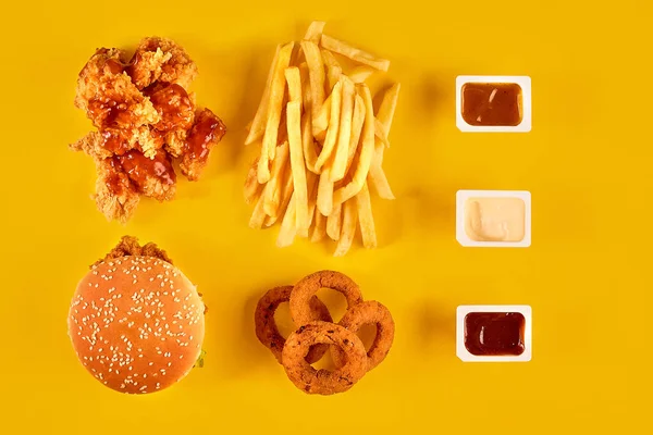 Pohled na rychlou občerstvení. Masový burger, bramborové lupínky a klíny. Odstraňte kompozici. Hranolky, hamburger, majonéza a kečup omáčky na žlutém pozadí. — Stock fotografie