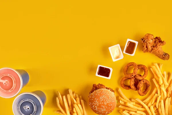 Piatto fast food vista dall'alto. Hamburger di carne, patatine fritte e cunei. Togli la composizione. Patatine fritte, hamburger, maionese e salse al ketchup su fondo giallo. — Foto Stock