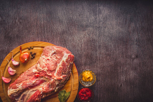 Raw pork on a chopping board on a dark wooden surface and spice for cooking. Food background with copy space. Toned