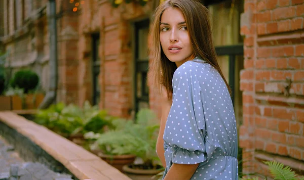 Menina loira em vestido azul longo e uma pequena bolsa preta em seu ombro está posando sentado de lado em um parapeito. Moda e estilo. Imagem de close-up. — Fotografia de Stock