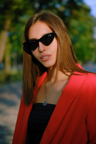 Kırmızı takım elbiseli ve siyah bluzlu sarışın kız, saat, yüzük, kolye ve güneş gözlüğü şehirde tek başına yürüyor. Moda ve tarz. Yakın plan.. — Stok fotoğraf