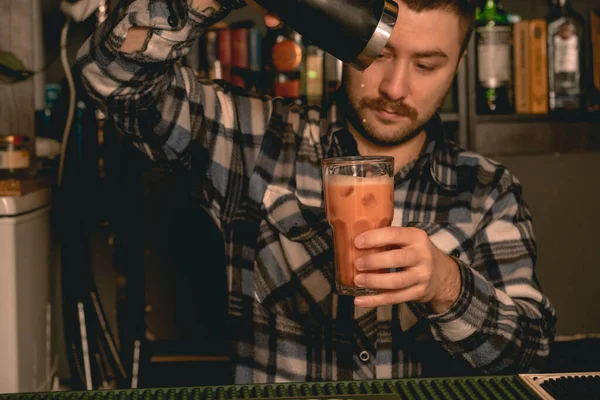 Bearded bartender pouring cocktail from shaker into highball glass — Stock Photo, Image