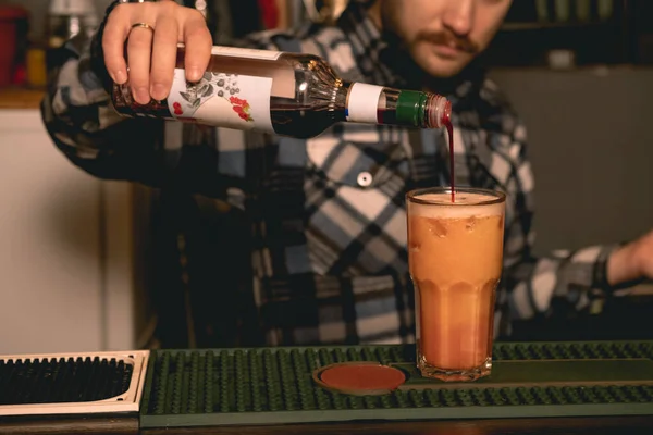 Бармен готовит коктейль "Текила Санрайз", добавляя гранатовый сироп в стакан с напитком — стоковое фото