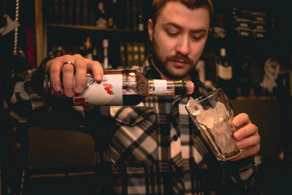 Cantinero vertiendo jarabe de granadina del frasco al vaso con hielo, preparando el cóctel Tequila Sunrise —  Fotos de Stock