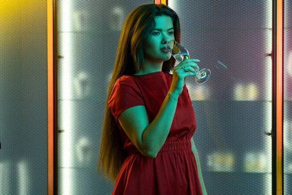 Stylish brunette enjoying sparkling wine in colored lighting of nightclub — ストック写真