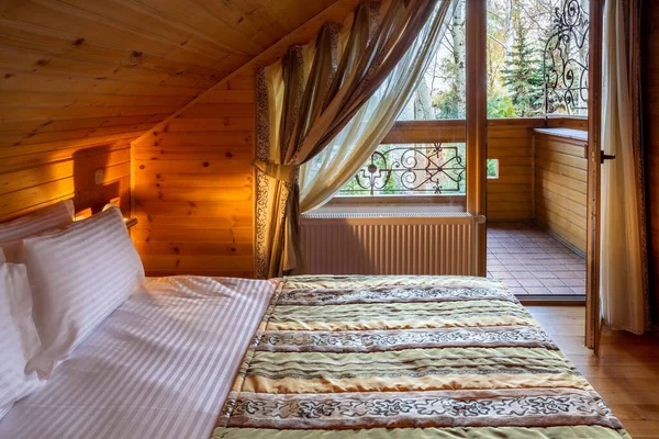 Przytulny mansard sypialnia z naturalnego drewna wykończenia z podwójnym łóżkiem i balkonem — Zdjęcie stockowe