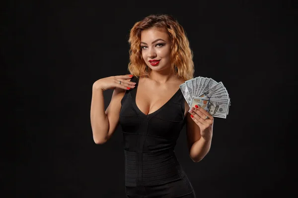 Τζίντζερ κορίτσι με σκούρο φόρεμα που ποζάρει κρατώντας φαν των εκατοντάδων δολαρίων στα χέρια της στέκεται πάνω από ένα μαύρο φόντο στούντιο. Καζίνο, πόκερ. Κοντινό πλάνο. — Φωτογραφία Αρχείου