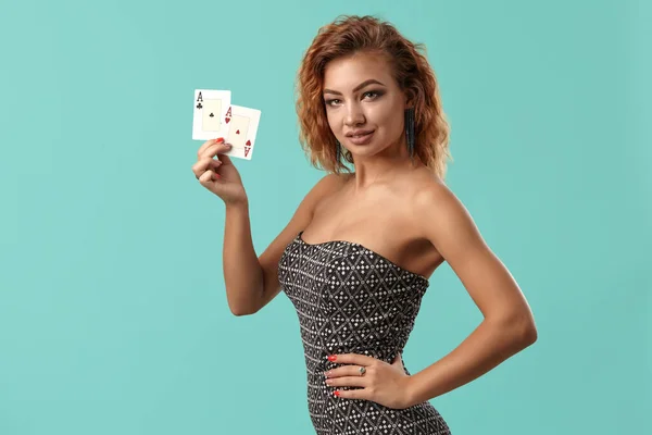 A szürke ruhás vörös lány pózol, két kártyajátékot tart a kezében, kék stúdió háttérrel szemben. Kaszinó, póker. Közelkép. — Stock Fotó
