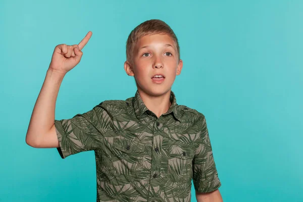 Close-up portrait of a blonde teenage boy in a green shirt with palm print posing against a blue studio background. Concept of sincere emotions. — Stockfoto