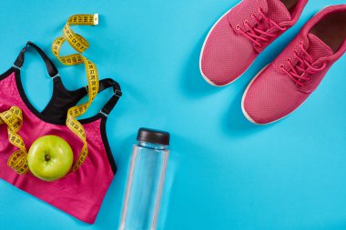 Cyan mavi arka planda mezuralı spor ayakkabılar. Sarı renkli santimetre, pembe spor ayakkabılar, kadın spor bluzu ve su şişesi, kopyalama alanı..