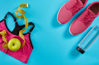 Cyan mavi arka planda mezuralı spor ayakkabılar. Sarı renkli santimetre, pembe spor ayakkabılar, kadın spor bluzu ve su şişesi, kopyalama alanı..