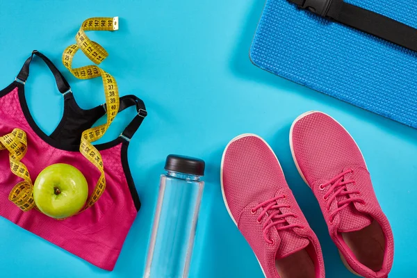 Turnschuhe mit Maßband auf cyanblauem Hintergrund. Zentimeter in gelb, rosa Turnschuhe, Sportoberteil und Wasserflasche für Frauen, Kopierraum. — Stockfoto