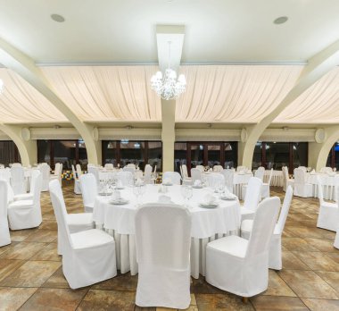 Yuvarlak servis masaları beyaz masa örtüleri ve beyaz örtülerle kaplı sandalyeler kristal avizelerle aydınlatılmış geniş ziyafet salonlarında düzenlenir, düğün resepsiyonu veya şenlik kutlamaları için hazırlanır.