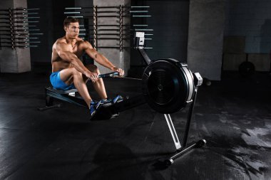 Vücut geliştirici spor salonunda ağırlık makinesiyle bacaklarının üzerinde çalışıyor. Mavi şortlu kaslı genç adam egzersiz yapıyor..