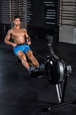 Vücut geliştirici spor salonunda ağırlık makinesiyle bacaklarının üzerinde çalışıyor. Mavi şortlu kaslı genç adam egzersiz yapıyor..