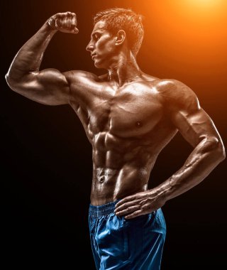 Siyah arka planda poz veren kaslı ve formda genç vücut geliştirici fitness erkek modeli. Stüdyo çekimi siyah arka planda. Güneş parlamasıyla