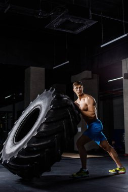 Spor salonunda lastik çeviren bir adam. Kaslı bir adam büyük bir lastiği itiyor.