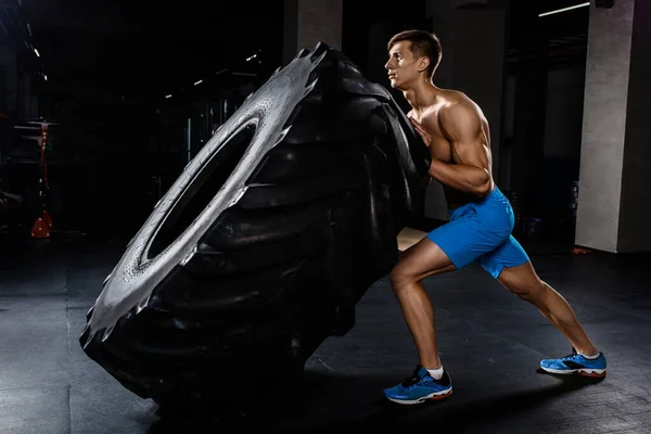 training - man flipping tire in gym. A muscular man pushes a big tire
