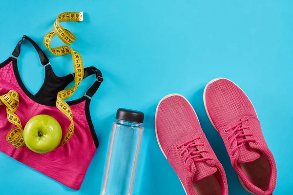 Cyan mavi arka planda mezuralı spor ayakkabılar. Sarı renkli santimetre, pembe spor ayakkabılar, kadın spor bluzu ve su şişesi, fotokopi alanı.. Spor ayakkabıları ve sağlıklı formda spor malzemeleri.
