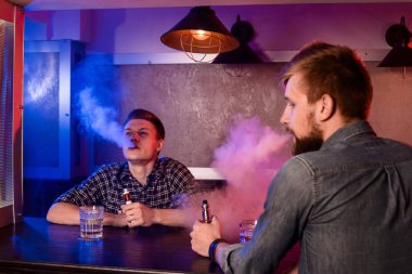 İki genç adam bir vapebar 'da elektronik sigara içiyor. Vestiyer.