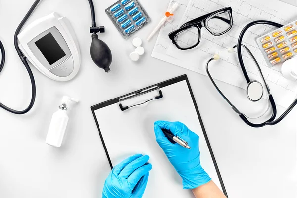 Doctor s table, tools, medical instruments, therapist tonometer, blood pressure, work in hospital on white background flat lay. The doctors hand in a blue glove records the indicators on a white