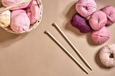 İplik topları. Hasır bir çanakta renkli iplik yumakları. Bej arka planda örgü örmek için iplik. Örgü örmek bir çeşit dikiş işidir. Örgü iğneleri ve çok renkli iplikler parlak görünüyor. Üst Manzara. Durgun hayat