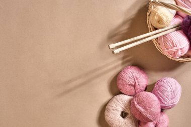 İplik topları. Hasır bir çanakta renkli iplik yumakları. Bej arka planda örgü örmek için iplik. Örgü örmek bir çeşit dikiş işidir. Örgü iğneleri ve çok renkli iplikler parlak görünüyor. Üst Manzara. Durgun hayat