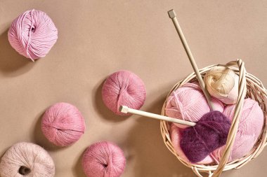 İplik topları. Hasır bir çanakta renkli iplik yumakları. Bej arka planda örgü örmek için iplik. Örgü örmek bir çeşit dikiş işidir. Örgü iğneleri ve çok renkli iplikler parlak görünüyor. Üst Manzara. Durgun hayat