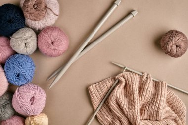 Renkli yün iplik seti ve bej arka planda örgü şişleri. Örgü örmek bir çeşit dikiş işidir. Renkli iplik topları ve örgü iğneleri. Üst Manzara. Durgun hayat. Uzayı kopyala Düz