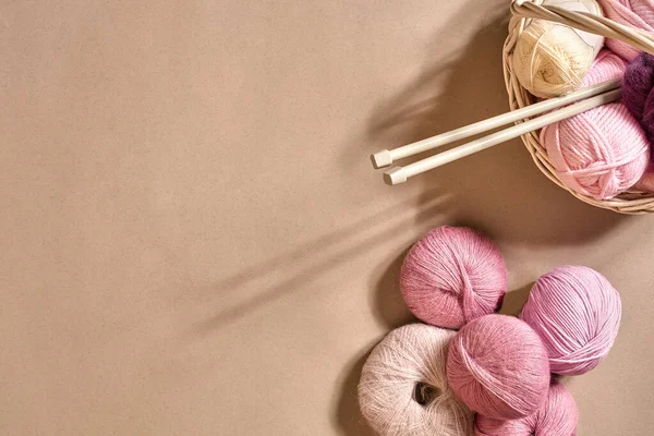 İplik topları. Hasır bir çanakta renkli iplik yumakları. Bej arka planda örgü örmek için iplik. Örgü örmek bir çeşit dikiş işidir. Örgü iğneleri ve çok renkli iplikler parlak görünüyor. Üst Manzara. Durgun hayat