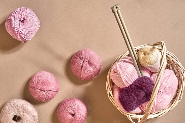 Yarn balls. Balls of colored yarn in a wicker dish. Yarn for knitting on a beige background. Knitting as a kind of needlework. Knitting needles and multi-colored yarn look bright. Top view. Still life