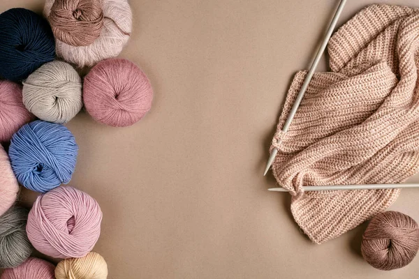 Set of colorful wool yarn and knitting on knitting needles on beige background. Knitting as a kind of needlework. Colorful balls of yarn and knitting needles. Top view. Still life. Copy space. Flat