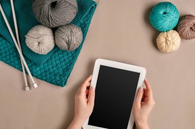 Gri ve turkuaz örgü yünü, örgü iğneleri ve bej arka planda siyah ekranlı bir tablet. Örgü örmek bir çeşit dikiş işidir. Renkli iplik topları ve örgü iğneleri. Üst Manzara. Devam et