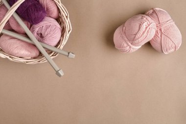 İplik topları. Hasır bir çanakta renkli iplik yumakları. Bej arka planda örgü örmek için iplik. Örgü örmek bir çeşit dikiş işidir. Örgü iğneleri ve çok renkli iplikler parlak görünüyor. Üst Manzara. Durgun hayat