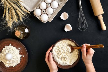 Kadınların elleri ev yapımı çiğ erişte, Rustik, Seçici Odak, Atmosferik Koyu Ton hazırlıyor. Mutfak masasının arkasında besin düzlüğü vardı. Un, yumurta ve yağla çalışıyor. Hamur işi mi fırın mı?