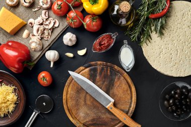 Tahta kesme tahtası ve geleneksel pizza hazırlama malzemeleri: peynir, domates sosu, fesleğen, zeytinyağı, biber, baharatlar. Siyah desenli masa arkaplanı. Üst Manzara. Durgun hayat. Uzayı kopyala Düz