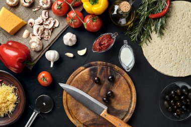Tahta kesme tahtası ve geleneksel pizza hazırlama malzemeleri: peynir, domates sosu, fesleğen, zeytinyağı, biber, baharatlar. Siyah desenli masa arkaplanı. Üst Manzara. Durgun hayat. Uzayı kopyala Düz