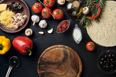 Tahta kesme tahtası ve geleneksel pizza hazırlama malzemeleri: peynir, domates sosu, fesleğen, zeytinyağı, biber, baharatlar. Siyah desenli masa arkaplanı. Üst Manzara. Durgun hayat. Uzayı kopyala Düz
