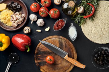 Tahta kesme tahtası ve geleneksel pizza hazırlama malzemeleri: peynir, domates, sos, zeytin, zeytin yağı, biber, baharatlar. Siyah desenli masa arkaplanı. Üst Manzara. Durgun hayat. Uzayı kopyala Düz