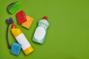 Orijinal deterjanlar ve temizlik aksesuarları, örneğin renkli süngerler, dezenfektan, boş etiketli bulaşıklar için temizleyici ve yeşil arka planda iki fırça. Temizlik, küçük işletme.