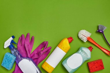 Modern deterjanlar ve temizlik aksesuarları, örneğin: boş etiketli bulaşıklar için sprey ve temizleyici, fırçalar, yeşil arka planda mor lastik eldivenler. Temizlik hizmeti, küçük