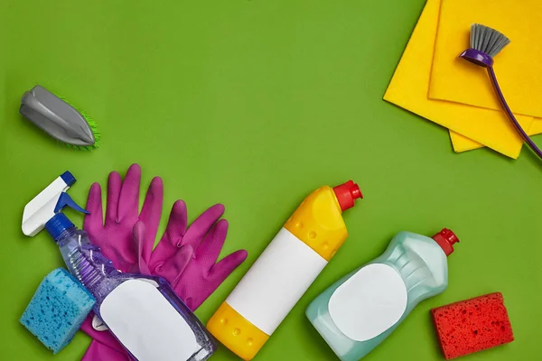 Modern detergents and cleaning accessories, such as: colorful sponges, spray and cleanser for dishes with an empty label, two brushes, purple rubber gloves and dishcloths on a green background