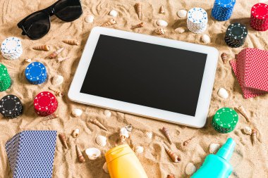 Online poker oyunu ile dijital tablet ve fiş destesi şeklinde sahilde. Üstten Görünüm. Uzay kopyalayın. Düz yatıyordu